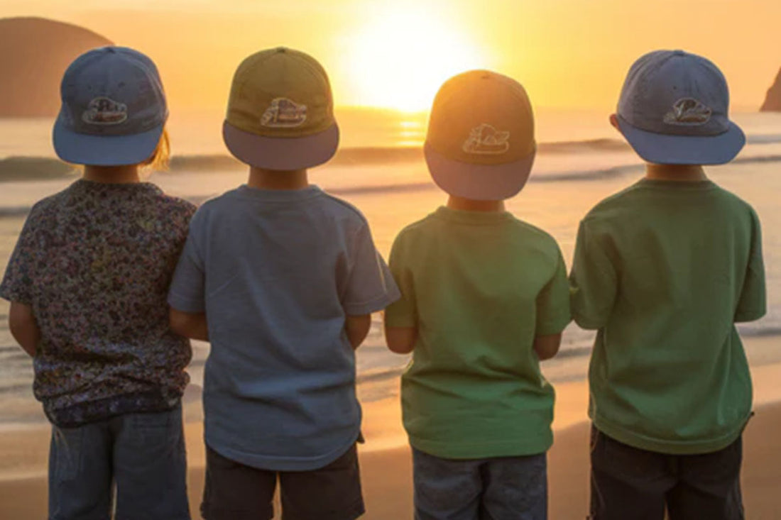 4 kids in sun hats stare at the sunset from a beach.