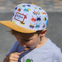 A kid in a cool printed space invaders hat eats some ice cream.